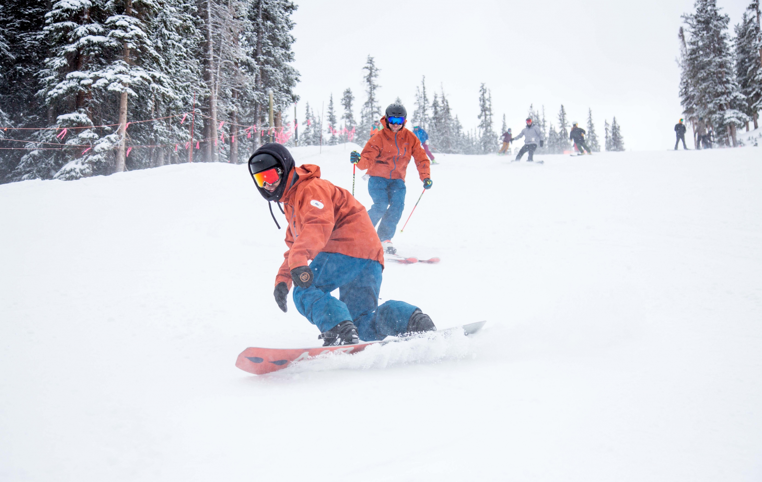 PSIA-AASI National Team members snowboard and ski down the slope at A-Basin