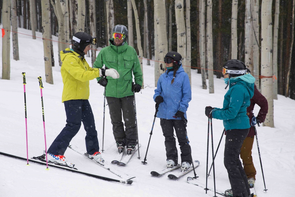 An alpine instructor gives a lesson to a group of three students on the hill