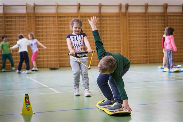 One student pulls another on a Burton Riglet board in their gym class