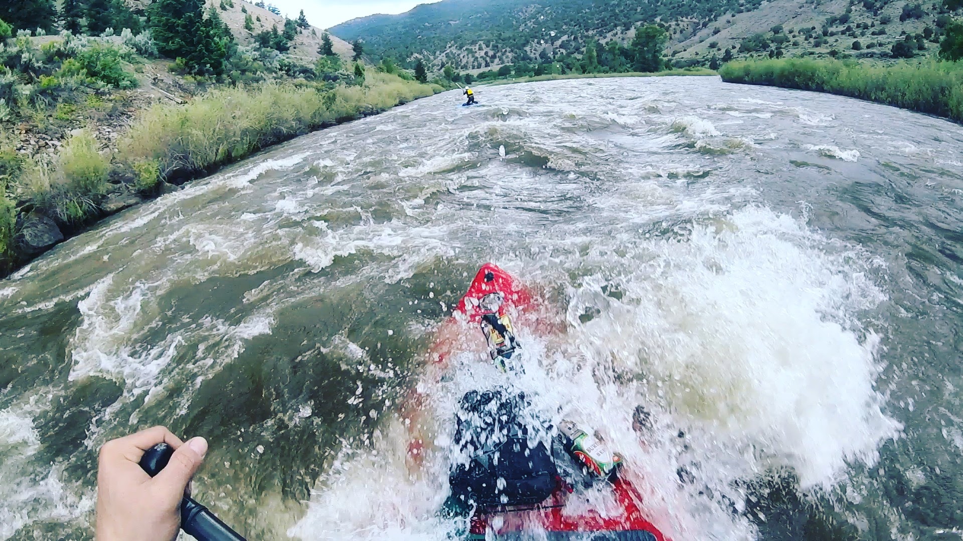 A stand up paddleboarder paddles over a river rapid.