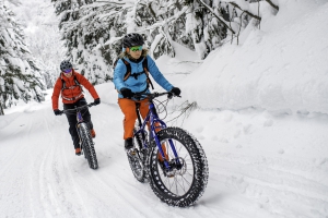 Two people snow bike down a trail