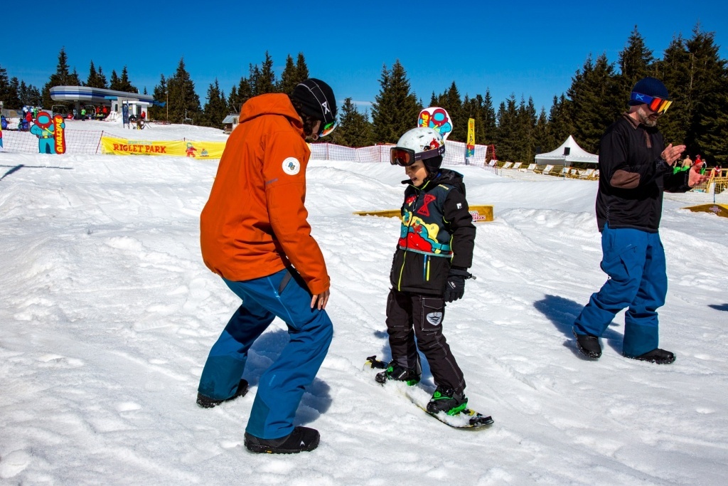 a snowboarder teaches a kid to snowboard at interski 2019