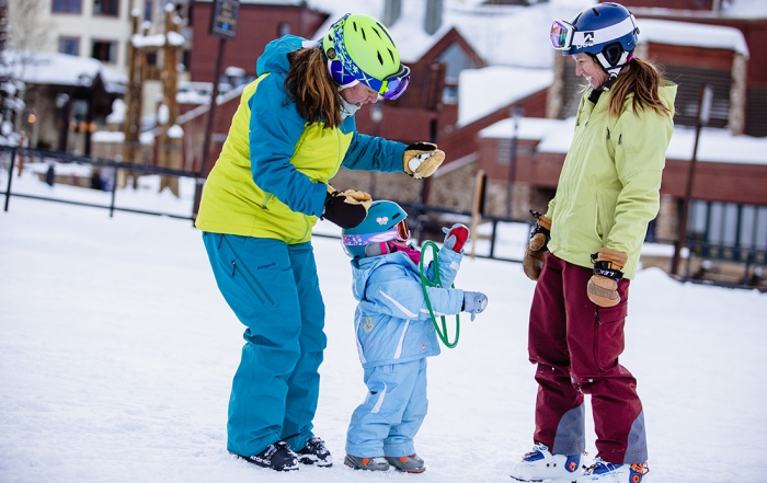 A ski instructor and mother and daughter work together at the base of a ski slope
