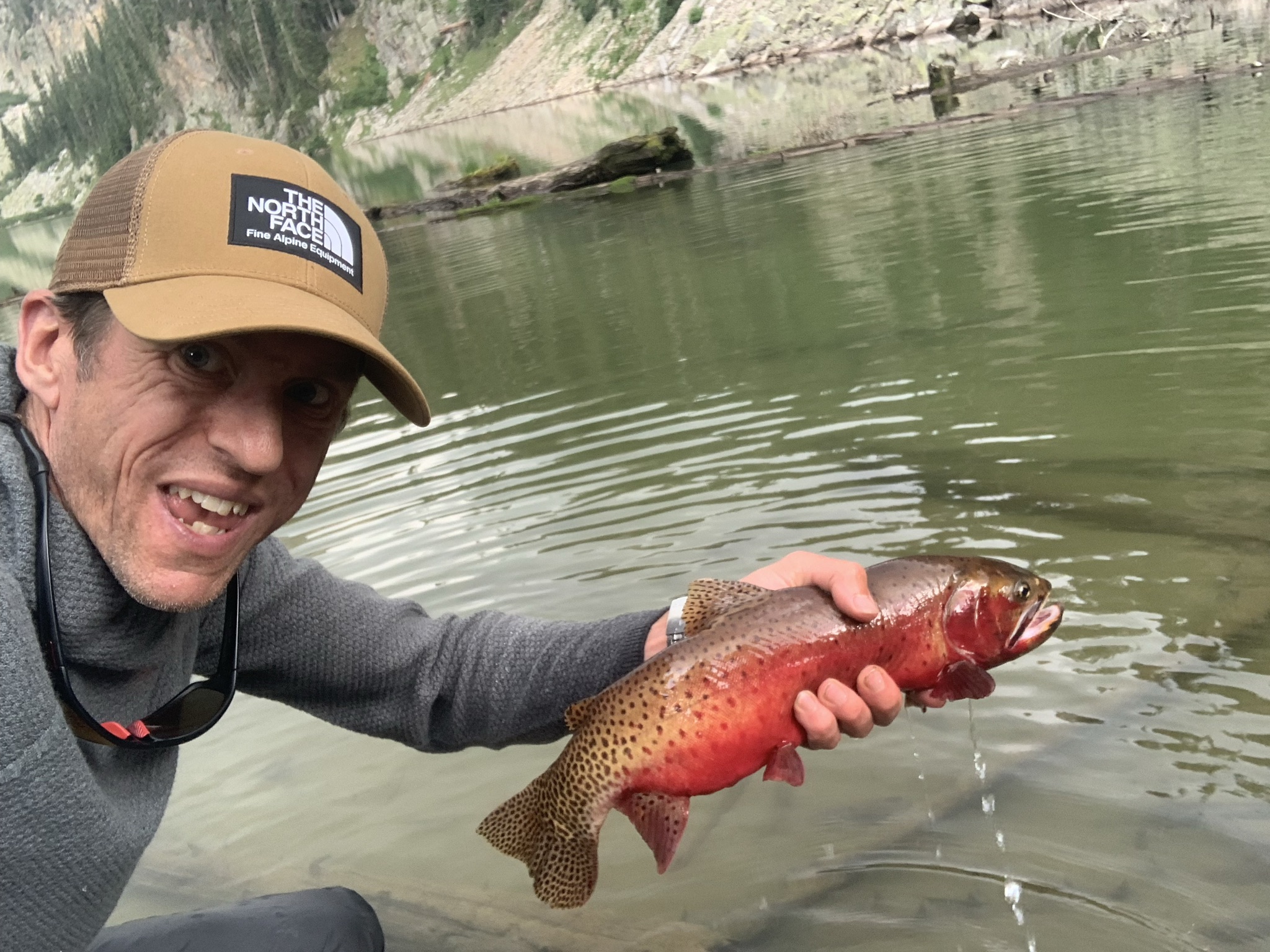 Joshua Fogg holds a trout in his hand while fly fishing